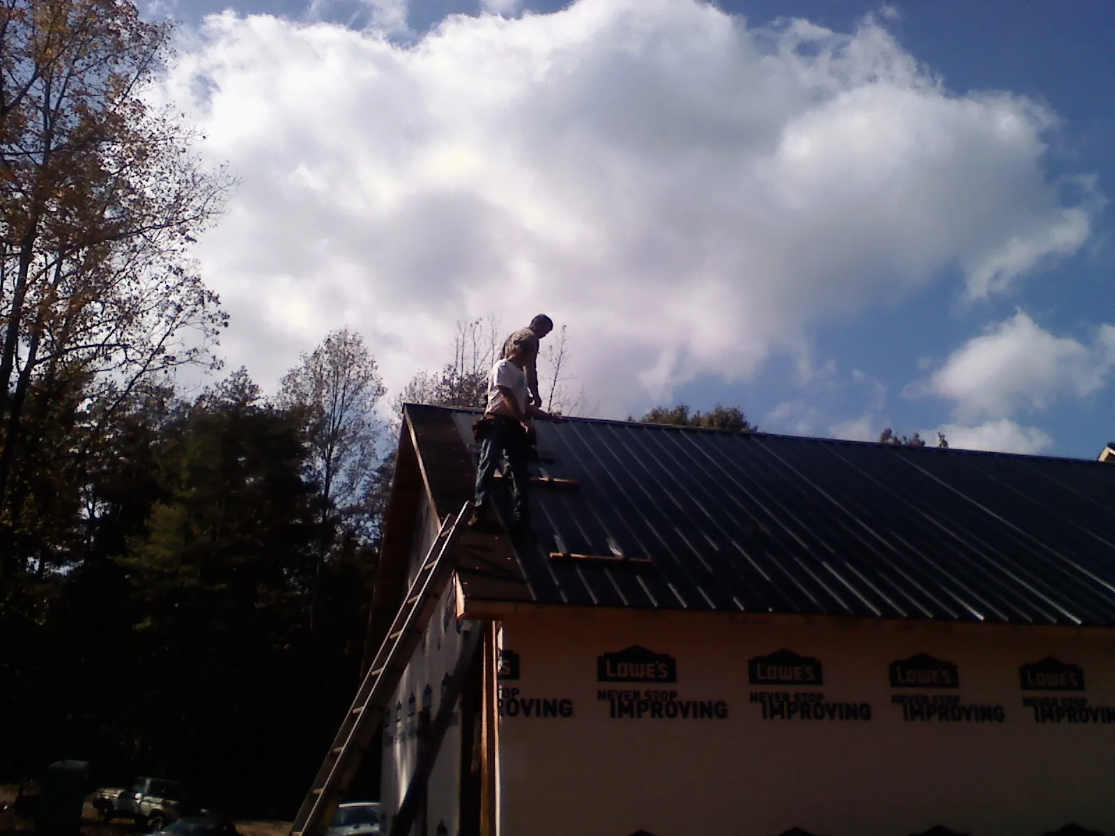 Roofer fastening dark metal panels high against a cloudy sky, from a Roof Inspection job in Azle